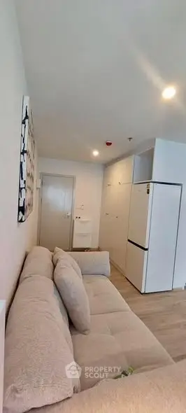 Modern living room with cozy beige sofa and sleek white refrigerator in a stylish apartment.