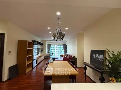 Spacious living room with elegant chandelier and city view, featuring hardwood floors and modern furnishings.