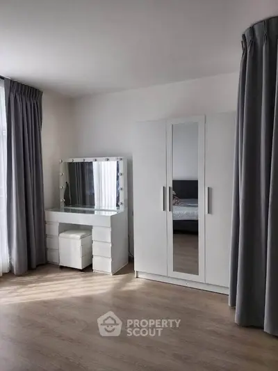 Spacious bedroom with modern wardrobe and vanity set, featuring elegant gray curtains.