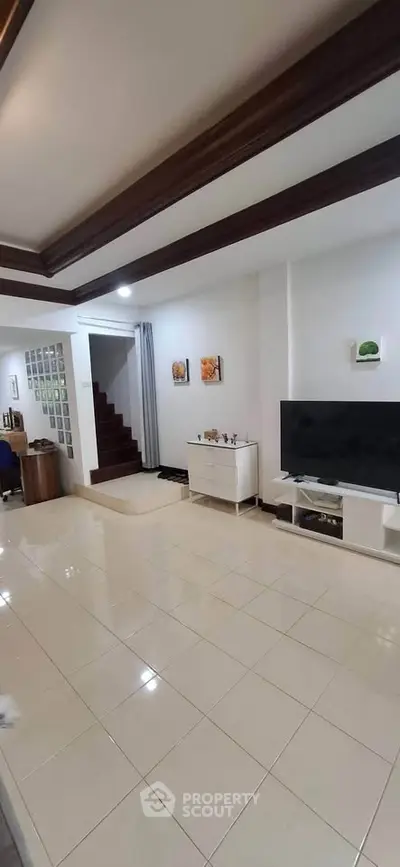 Spacious living room with modern decor and large TV, featuring elegant ceiling design and tiled flooring.