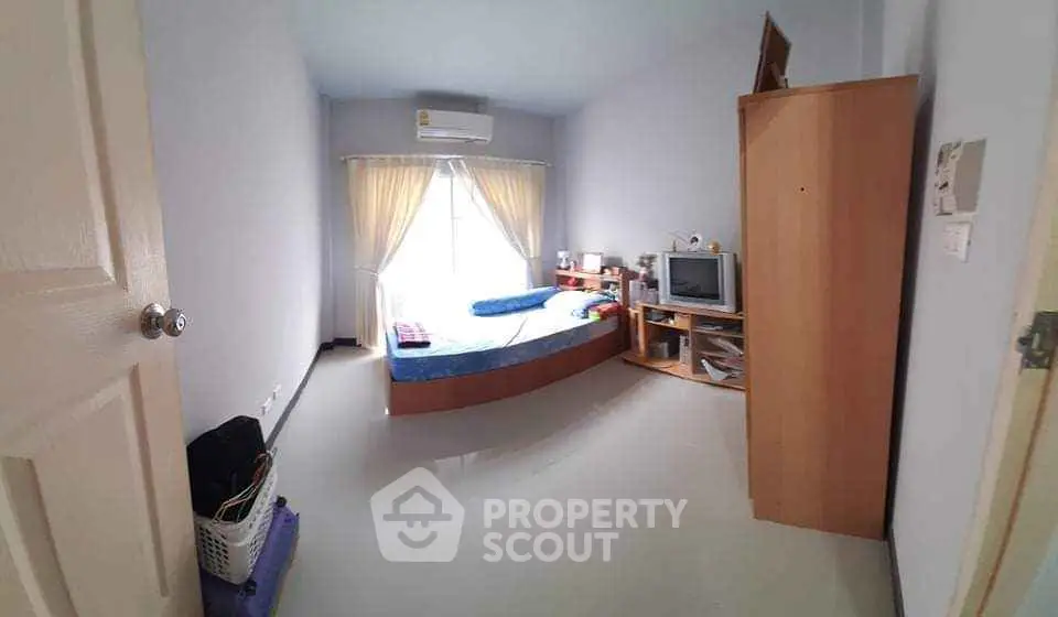 Cozy bedroom with natural light, featuring a bed, TV, and wardrobe for comfortable living.