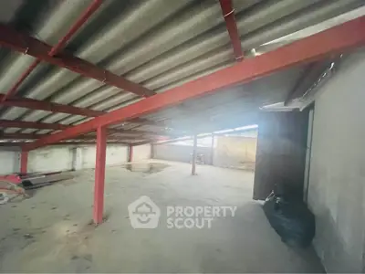 Spacious industrial-style storage area with metal roof and red beams, ideal for warehouse use.