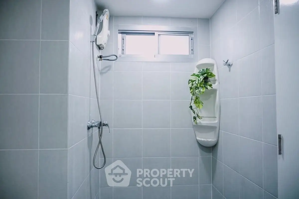 Modern bathroom with sleek gray tiles and a stylish shower area, featuring a decorative plant for a fresh touch.