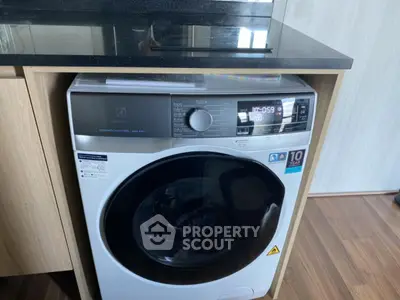 Modern washing machine in sleek kitchen interior with wooden cabinetry and dark countertop.