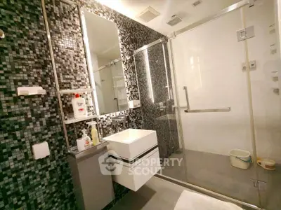 Modern bathroom with sleek glass shower and mosaic tile wall design.