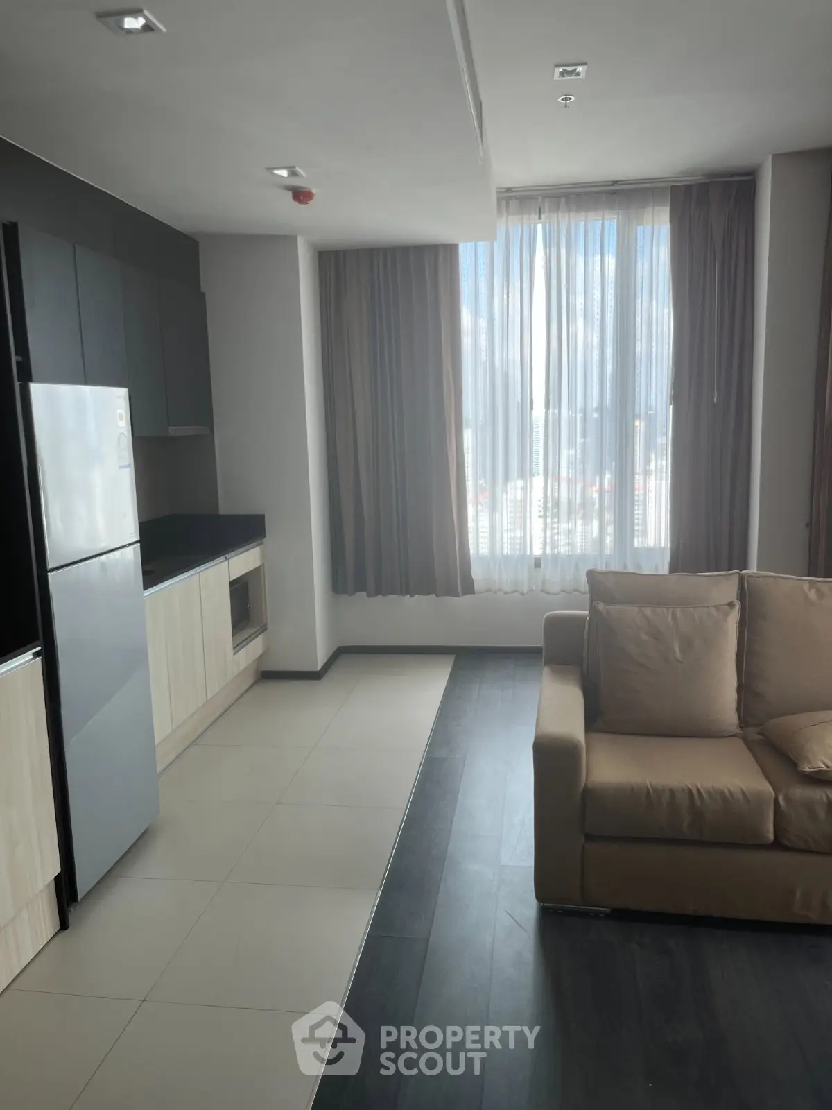 Modern apartment interior with sleek kitchen and cozy living area, featuring large windows and natural light.