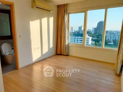 Bright room with wooden flooring and large windows offering city views, adjacent to a modern bathroom.