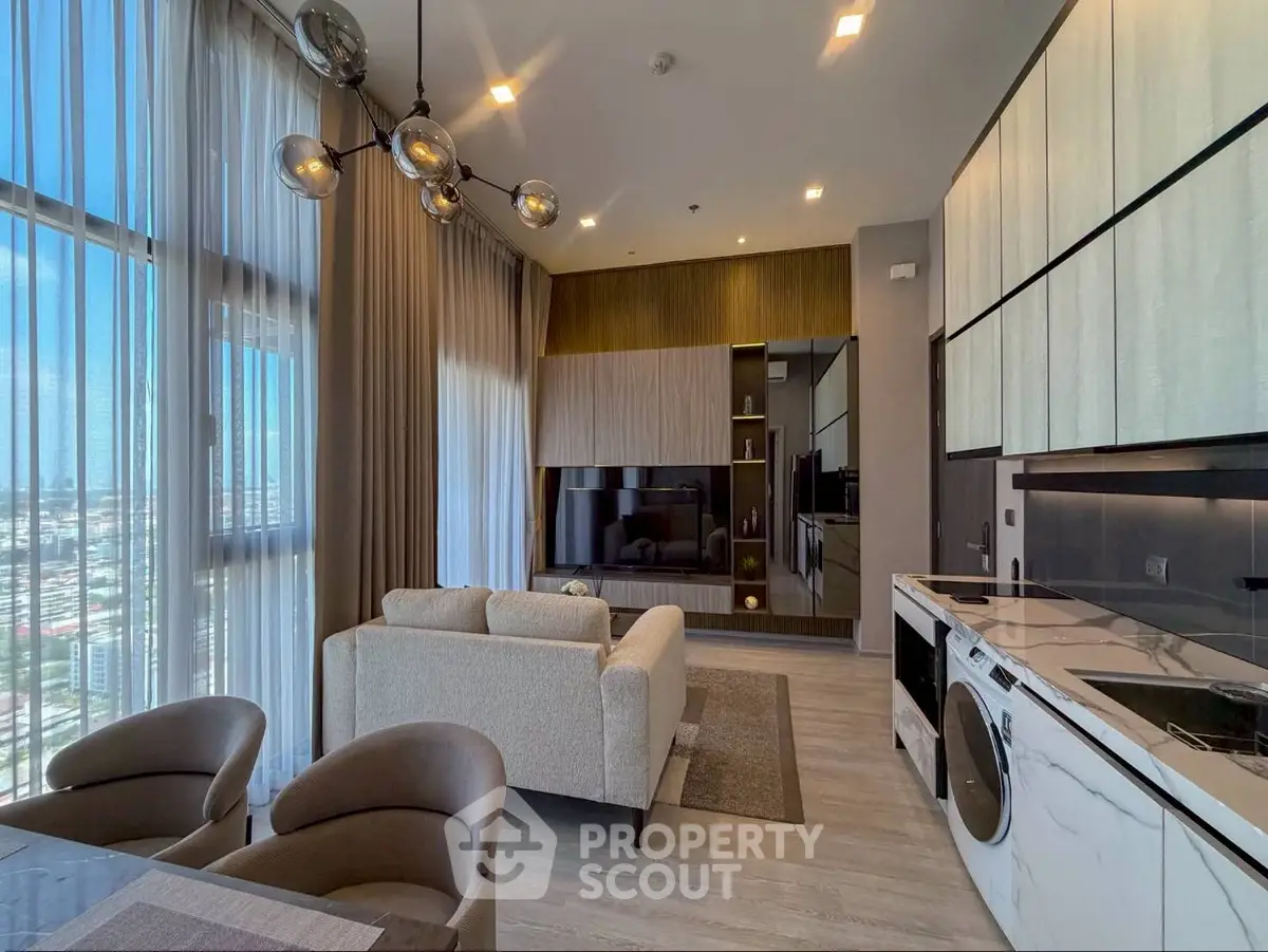 Modern open-layout living room with kitchen, featuring sleek design and large windows offering city views.
