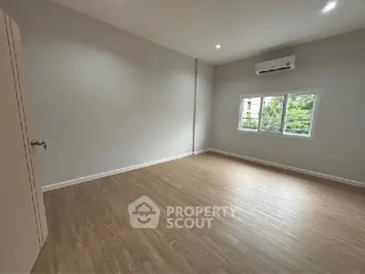 Spacious empty room with wooden flooring and air conditioning, ready for customization.