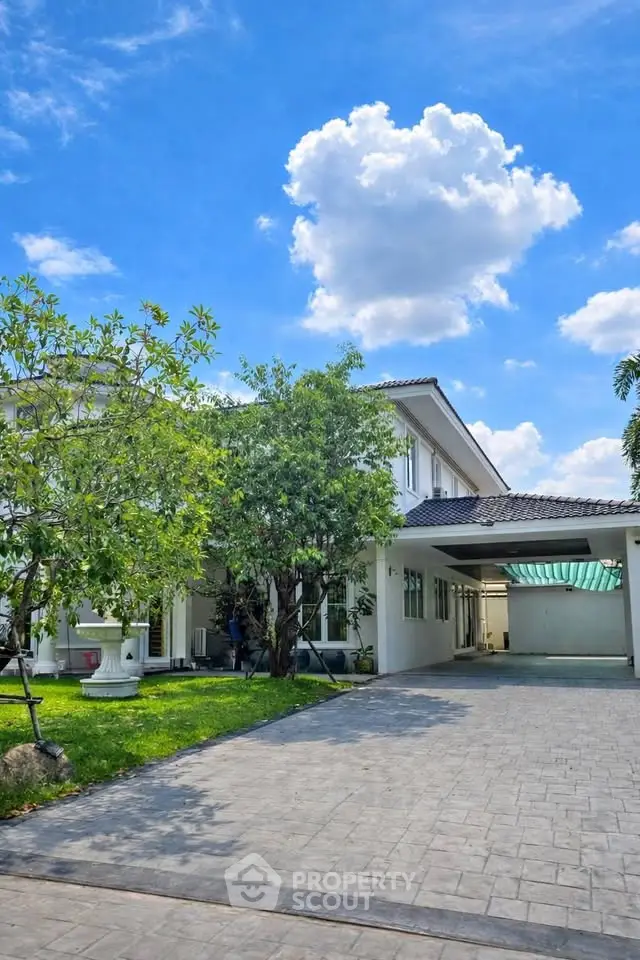 Charming two-story house with lush garden and spacious driveway under a bright blue sky.