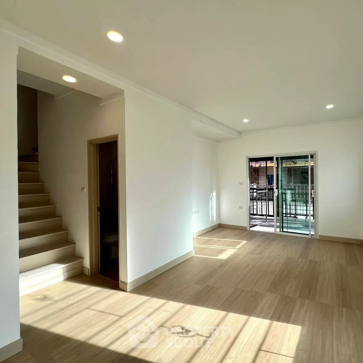 Bright and spacious living room with wooden flooring and large windows leading to a balcony.