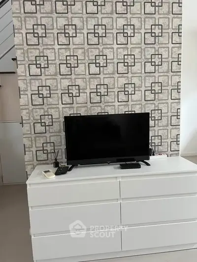 Modern living room with stylish wallpaper and sleek TV setup on white dresser.