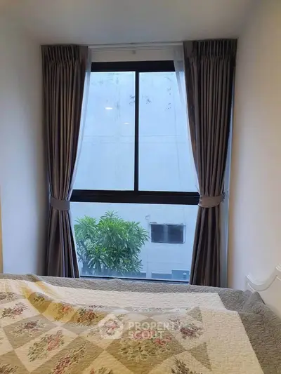Cozy bedroom with large window and elegant curtains offering a serene view of greenery outside.