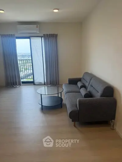 Spacious living room with modern sofa and glass coffee table, featuring a large window with a stunning view.