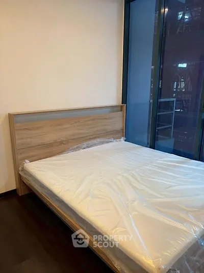 Modern bedroom with large window and new bed frame in urban apartment.