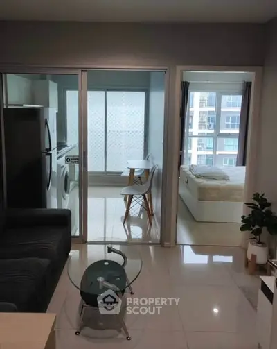 Modern apartment with open living area, glass table, and bedroom view.