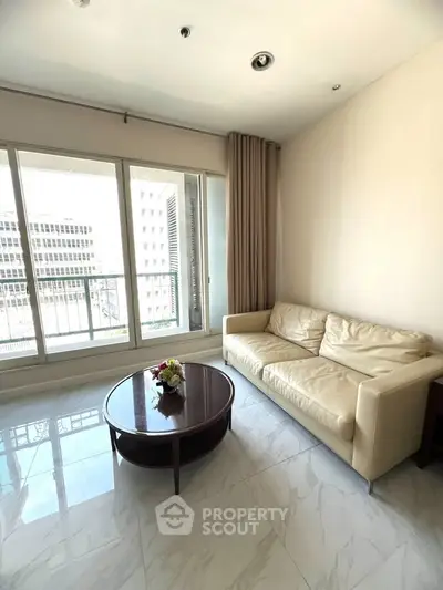 Bright living room with modern sofa and coffee table, featuring large windows and city view.