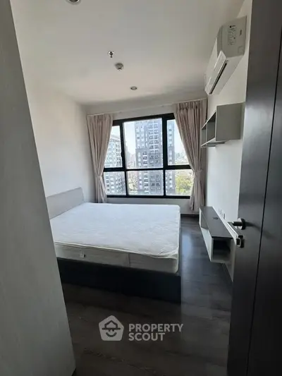 Modern bedroom with large window offering city view, featuring sleek furniture and air conditioning.