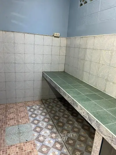 Simple tiled kitchen area with counter and patterned floor tiles.