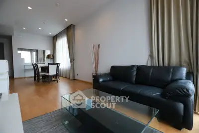 Spacious modern living room with sleek black leather sofa and elegant dining area.