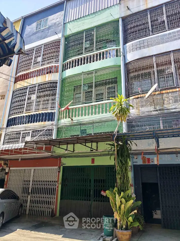 Colorful multi-story building with gated balconies and street-level parking in urban setting.