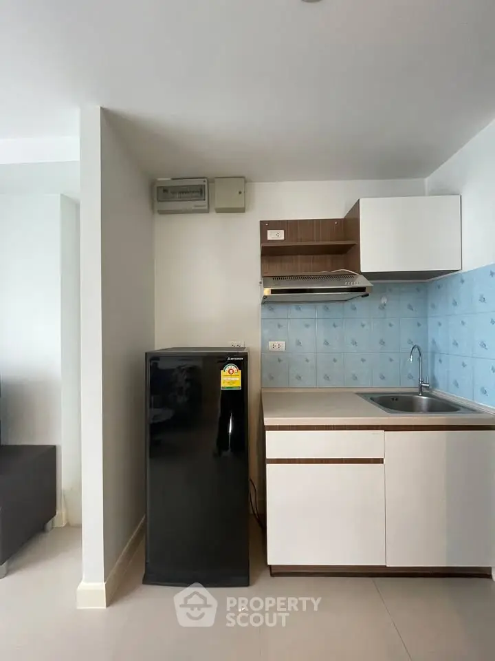 Modern kitchen with sleek black fridge and stylish cabinetry in compact apartment.