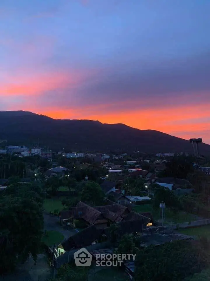 Stunning sunset view over a serene residential area with lush greenery and distant hills.
