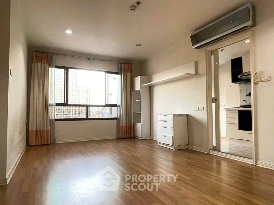 Spacious living room with wooden flooring and large window offering city views.