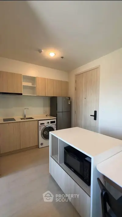 Modern kitchen with wooden cabinets, washing machine, and microwave in a compact apartment.