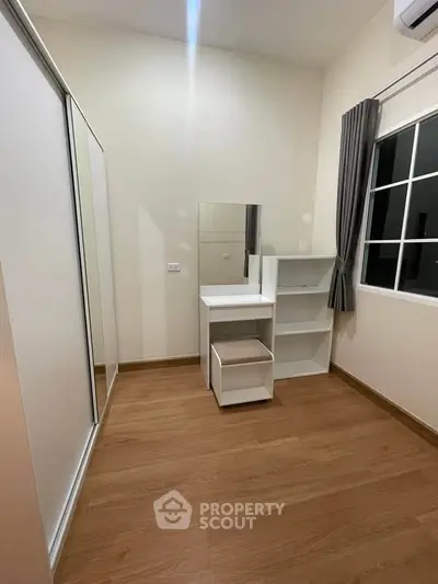 Modern bedroom with sleek furniture and wooden flooring, featuring a stylish vanity and ample natural light.