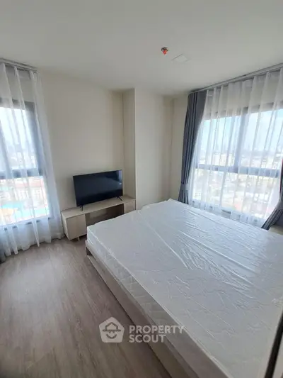 Modern bedroom with large windows and city view, featuring a sleek TV and minimalist decor.