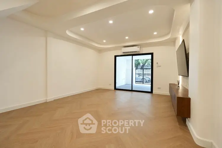 Spacious modern living room with wooden flooring and large window opening to a garden view.
