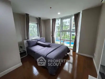 Spacious bedroom with pool view in modern apartment, featuring large windows and elegant decor.