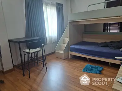 Modern bedroom with loft bed and study area, featuring wooden flooring and natural light.