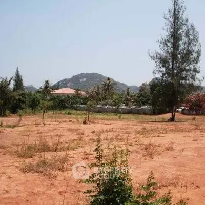 Expansive undeveloped land with rich red soil, set against a backdrop of lush greenery and distant hills, offering a serene and picturesque setting for a bespoke residential or commercial development.