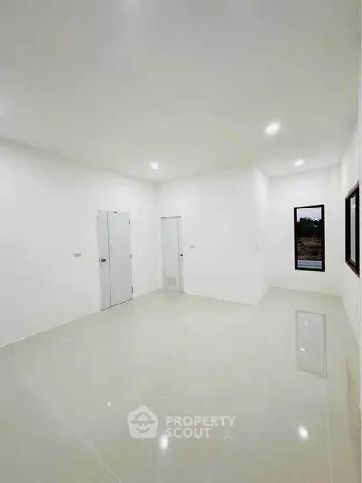 Spacious empty room with white walls and tiled floor, featuring large windows for natural light.