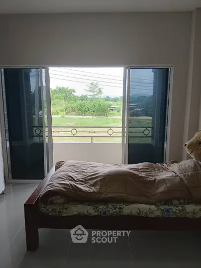 Spacious bedroom with balcony and scenic view of greenery.