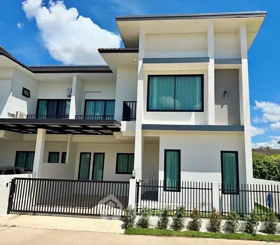 Modern two-story house with sleek design and large windows, featuring a gated entrance and lush greenery.