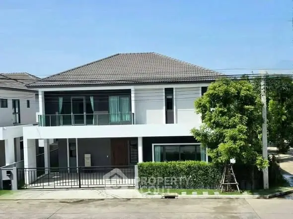 Modern two-story house with large windows and lush greenery in a serene neighborhood.