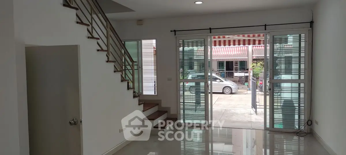 Spacious modern living room with large windows and staircase, perfect for natural light lovers.