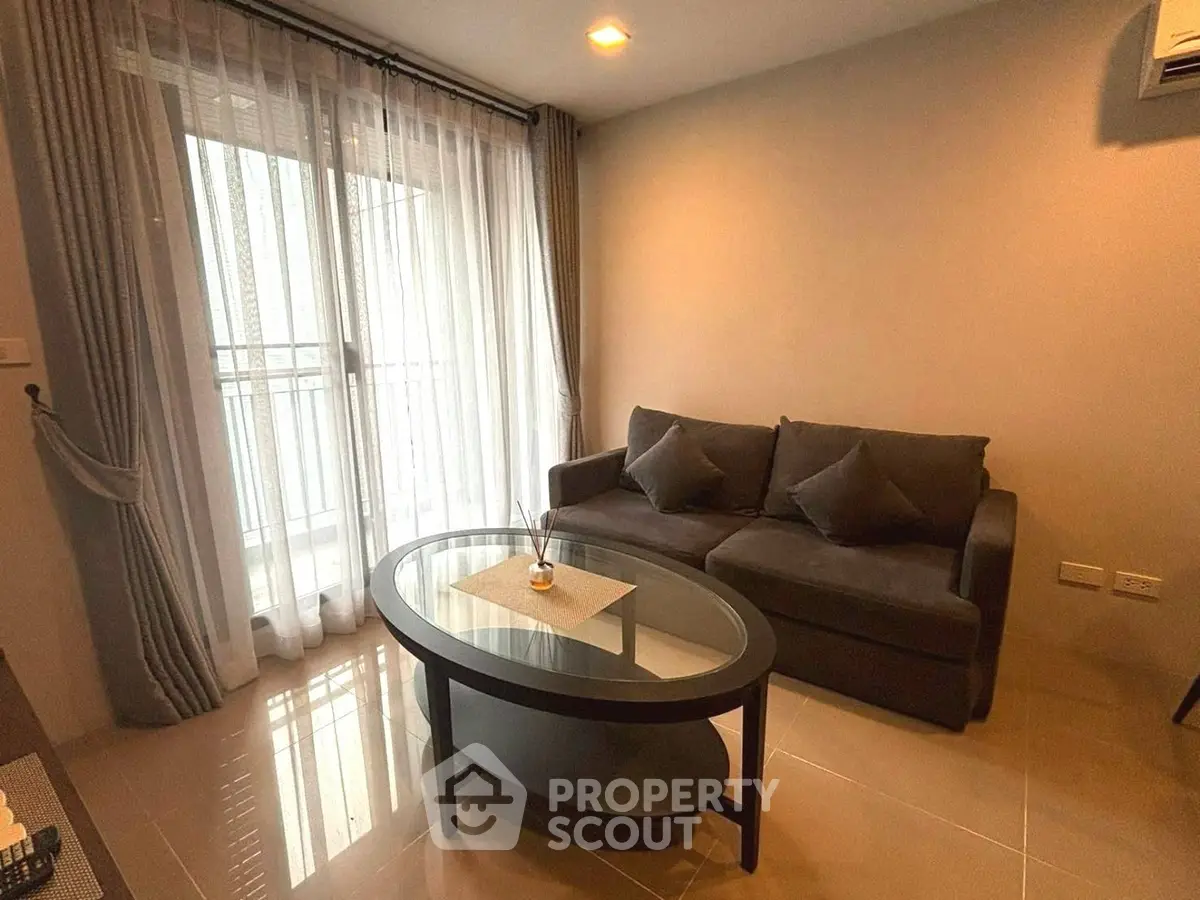 Cozy living room with modern sofa and glass coffee table, featuring floor-to-ceiling windows and elegant curtains.