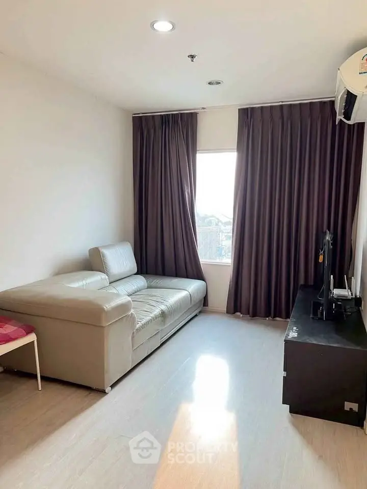 Cozy living room with modern sofa and entertainment unit, featuring natural light and elegant curtains.