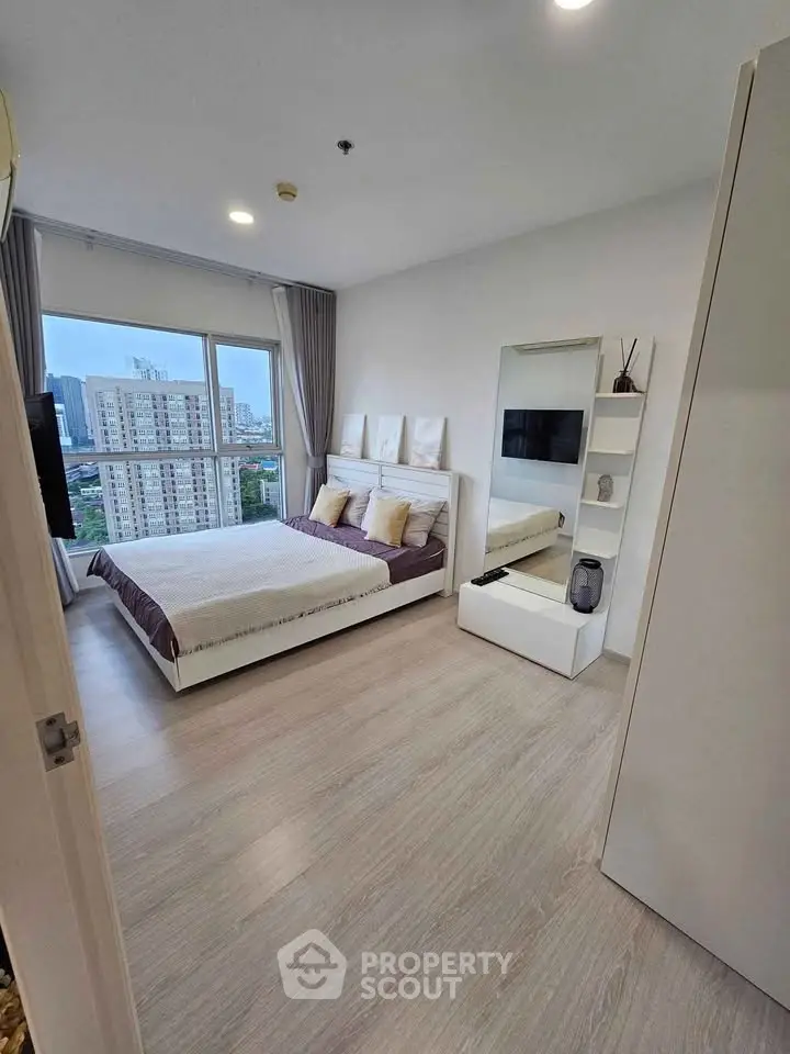 Modern bedroom with city view, featuring sleek furniture and large window for natural light.
