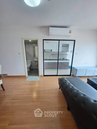 Modern living room with sleek kitchen and air conditioning, featuring stylish furniture and wooden flooring.