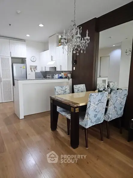 Elegant dining area with chandelier and modern kitchen in open layout apartment.