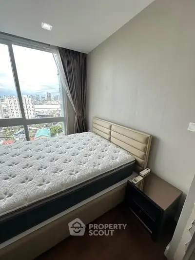 Modern bedroom with city view, featuring a plush bed and sleek nightstand, perfect for urban living.