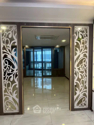 Elegant interior with decorative partition and spacious tiled floor, leading to a bright room with large windows.