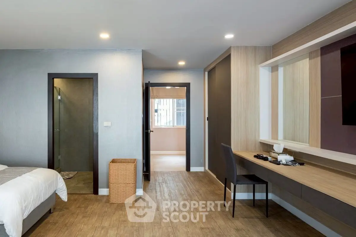 Modern bedroom with stylish decor and workspace, featuring wooden flooring and neutral tones.