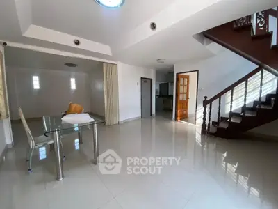 Spacious living room with modern glass table and elegant staircase in bright open layout.