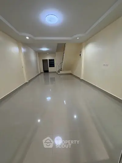 Spacious empty room with glossy tiled flooring and staircase, ideal for customization.